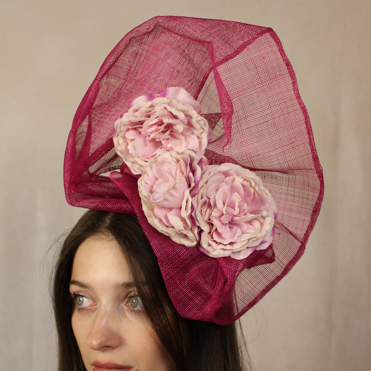 Woman wearing a pink hat with floral decorations against a neutral background.
Fuchsia statement hat with pale pink flowers, handmade by SJL Couture.