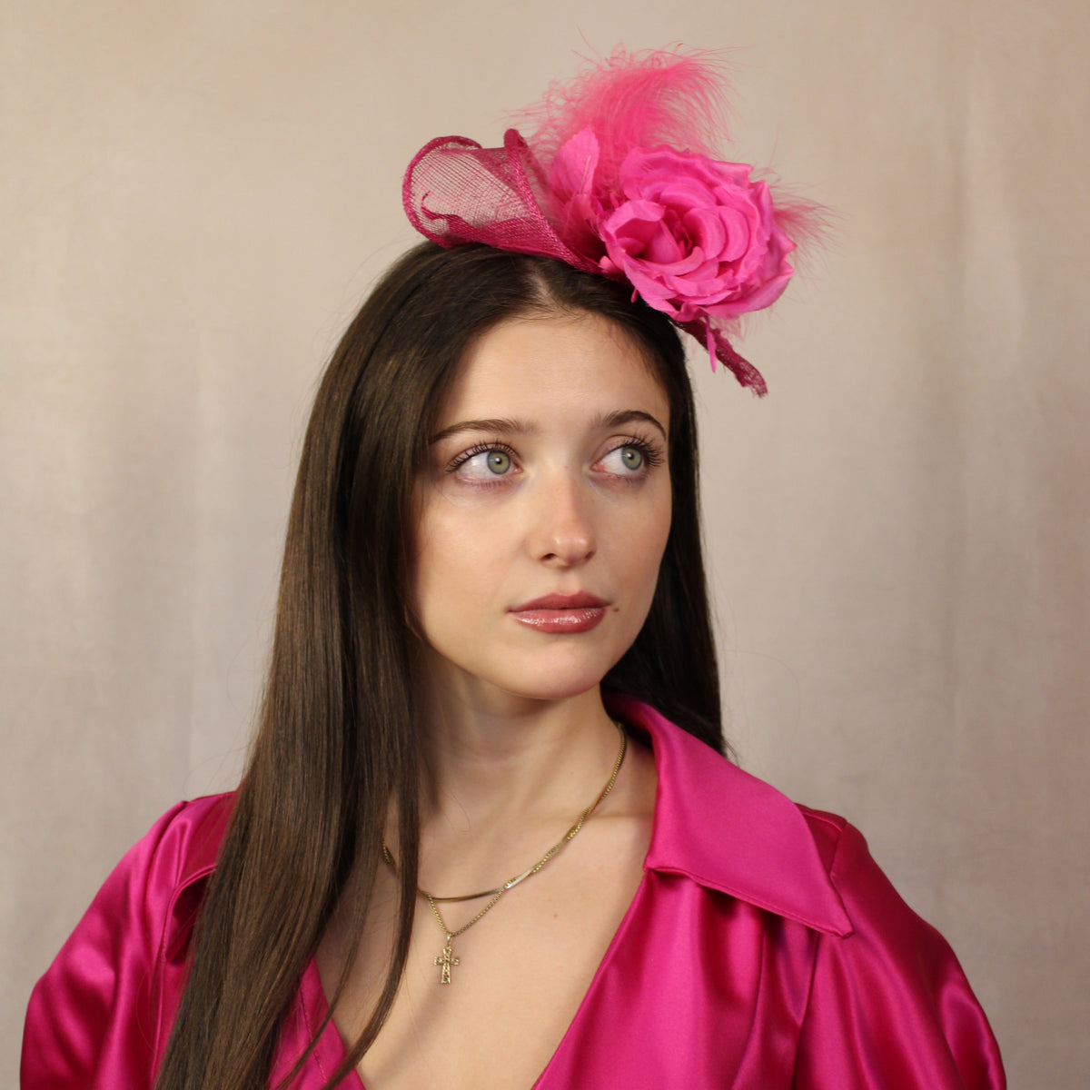 A woman wearing a fuchsia pink fascinator with a flower and feather detail in her hair. Fuchsia pink fascinator with flower and feather detail