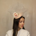 A woman wearing a pale pink headpiece with a head band, adorned with a rose and swirl crinoline.