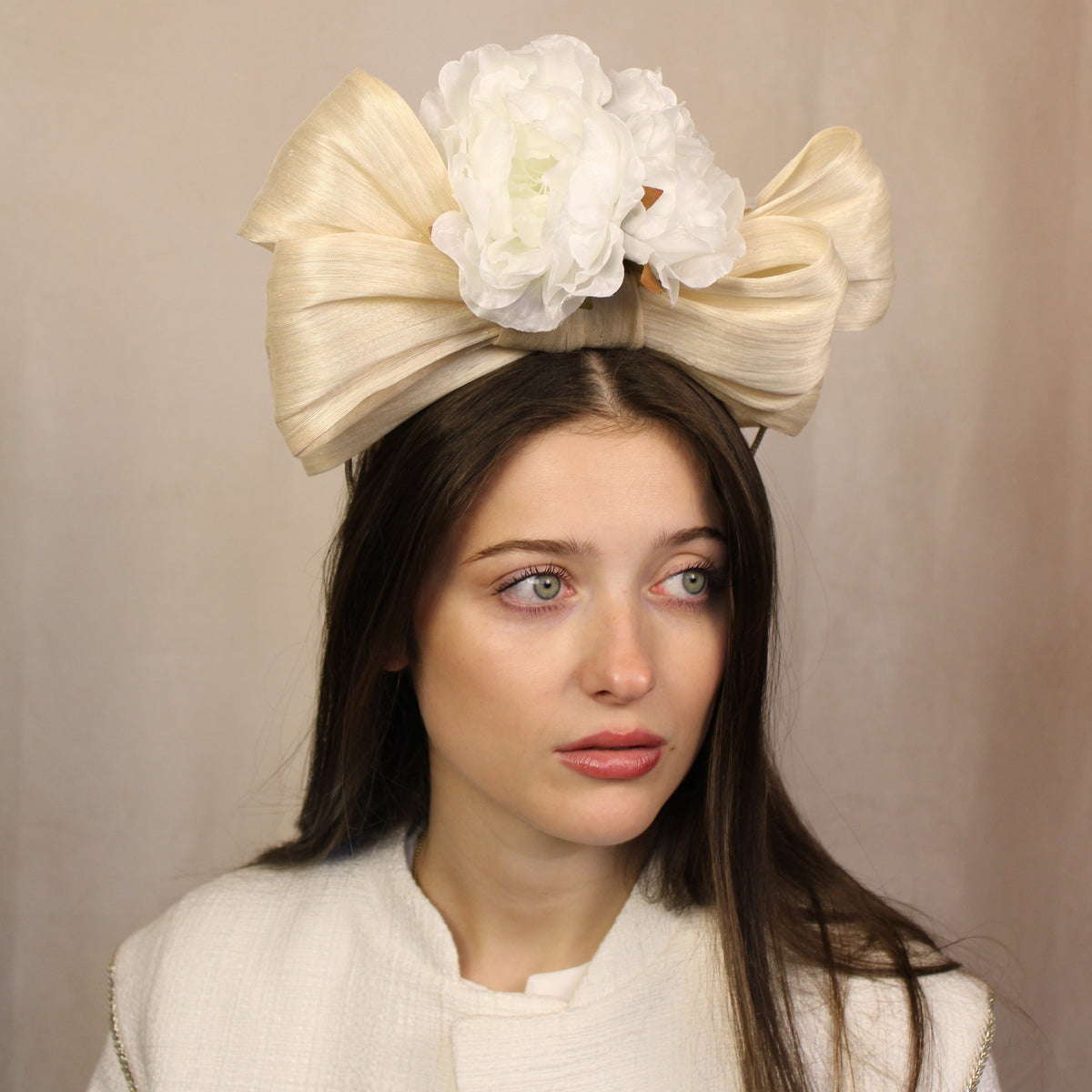A woman wearing a beige silk abaca bow headband with white flowers. Ivory silk abaca bow headband with white flowers, handmade by SJL Couture