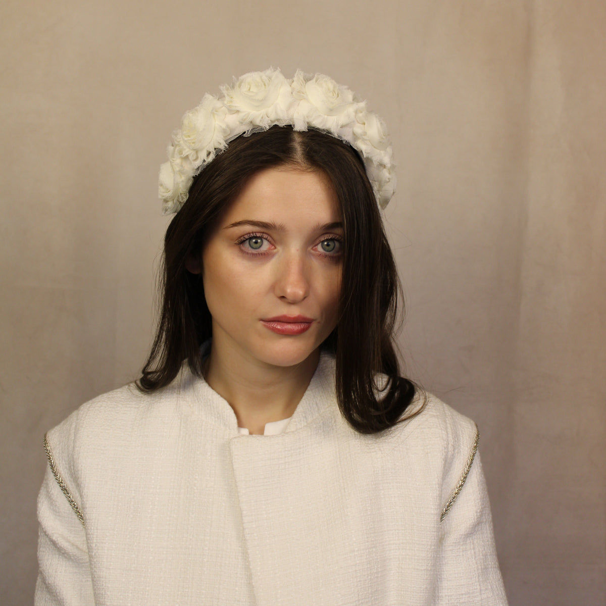 A woman wearing a white cream-padded headband with fabric flowers. Cream padded headband with fabric flowers, handmade by SJL Couture