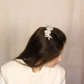 A woman with straight hair viewed from the back, wearing a white dress and a hair comb with white embroidered applique and diamante detailing on top.
