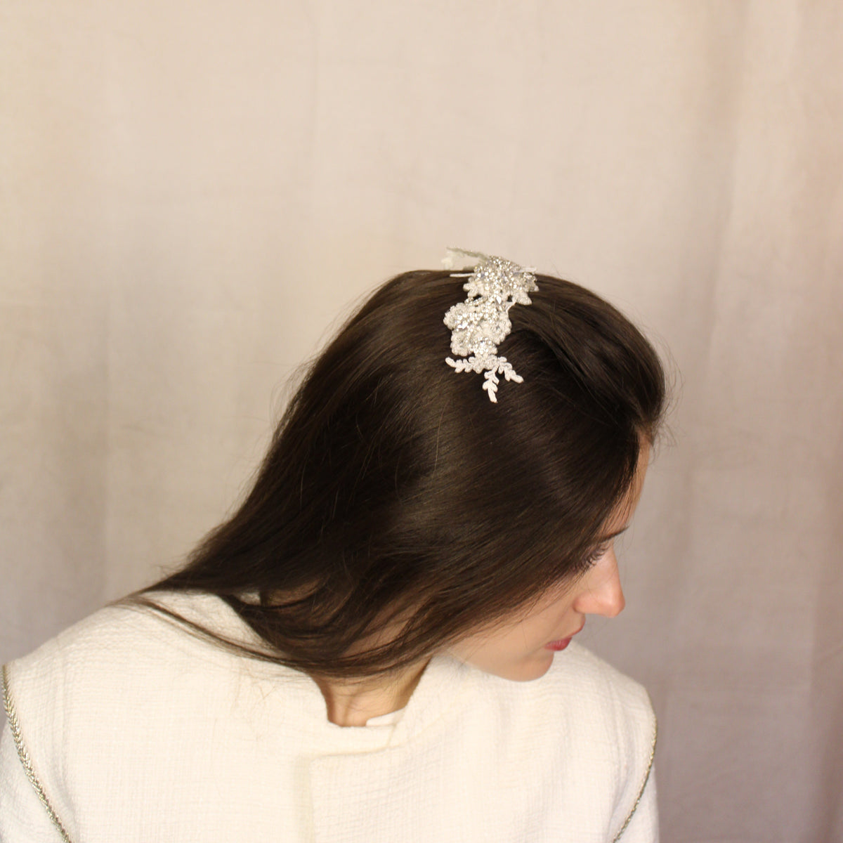 A woman with straight hair viewed from the back, wearing a white dress and a hair comb with white embroidered applique and diamante detailing on top.