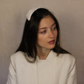 A woman wearing a white bridal gown and a white silk satin headpiece with hand sewn beads and lace, featuring an elastic attachment.