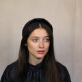 A person wearing a navy blue velour headband with a small bead detail. Navy velour headband with beads