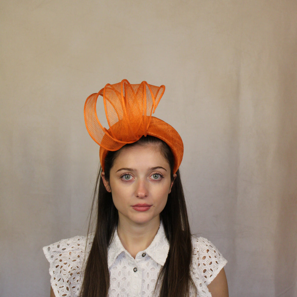 A woman wearing an orange halo headpiece with a sinamay straw swirl. Orange halo headpiece with a sinamay straw swirl.