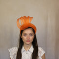 A woman wearing an orange halo headpiece with a sinamay straw swirl. Orange halo headpiece with a sinamay straw swirl.