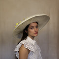 A woman wearing a cream and yellow wide-brimmed hat with vintage flowers, paired with a white lace top. Cream and yellow hat with vintage flowers and silk abaca