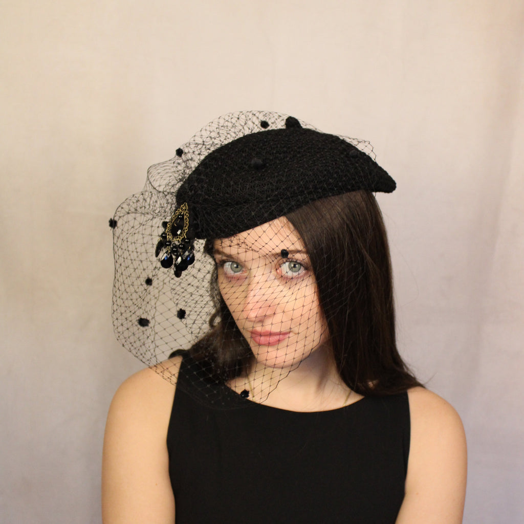 A woman wearing a black woven polyester beret with a black dotted crinoline and stone embellishments. Black woven beret with dotted crinoline veil and stone embellishment.
