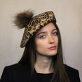 A woman wearing a brown and beige animal print wool beret with a brown pompom. Animal print wool beret in brown and beige with a brown pompom