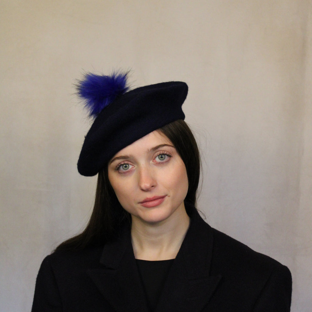 A woman wearing a navy blue wool beret with an indigo pompom. Navy blue wool beret with indigo pompom