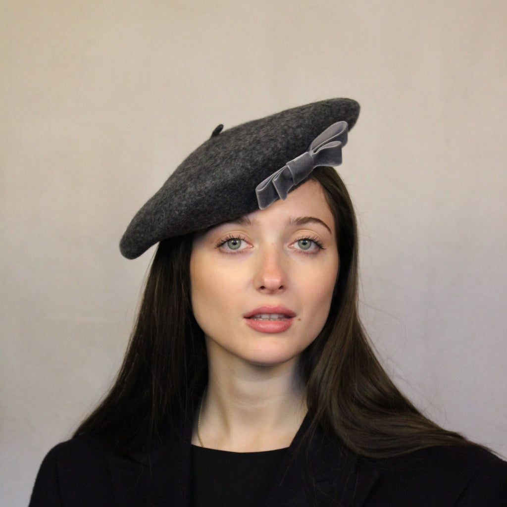 A woman wearing a gray wool beret with a velvet bow trim. Grey wool beret with velvet bow trim